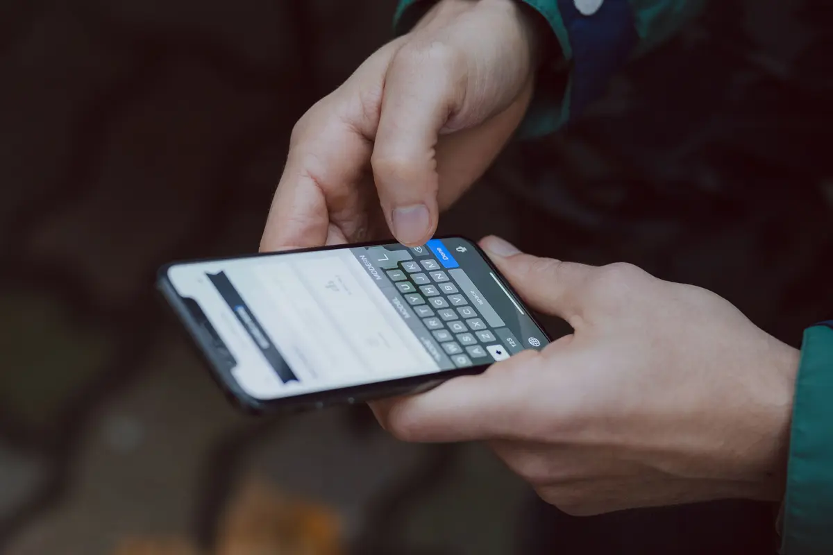 Two hands typing a message on a smartphone held sideways, keyboard visible on screen